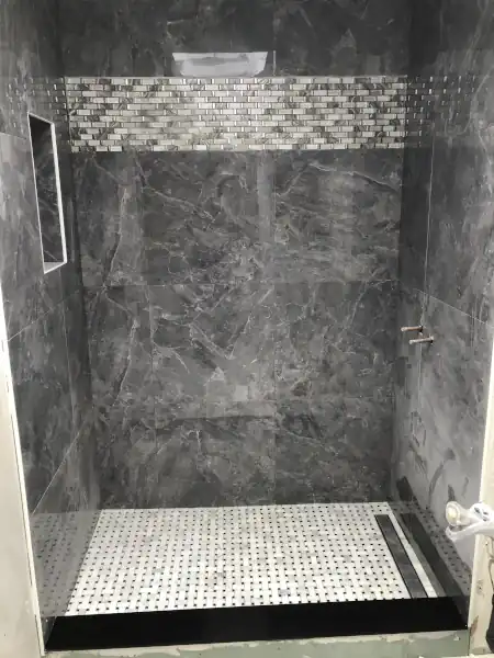 Finished shower with mosaic tile floor band and glass panel