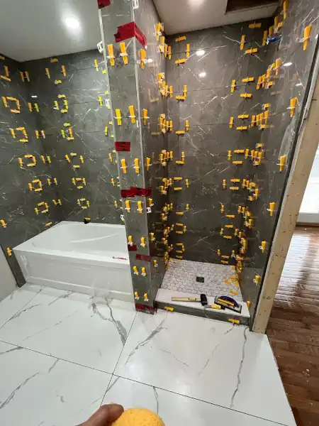 Marble tile shower with gold-tone fixtures, installation in progress